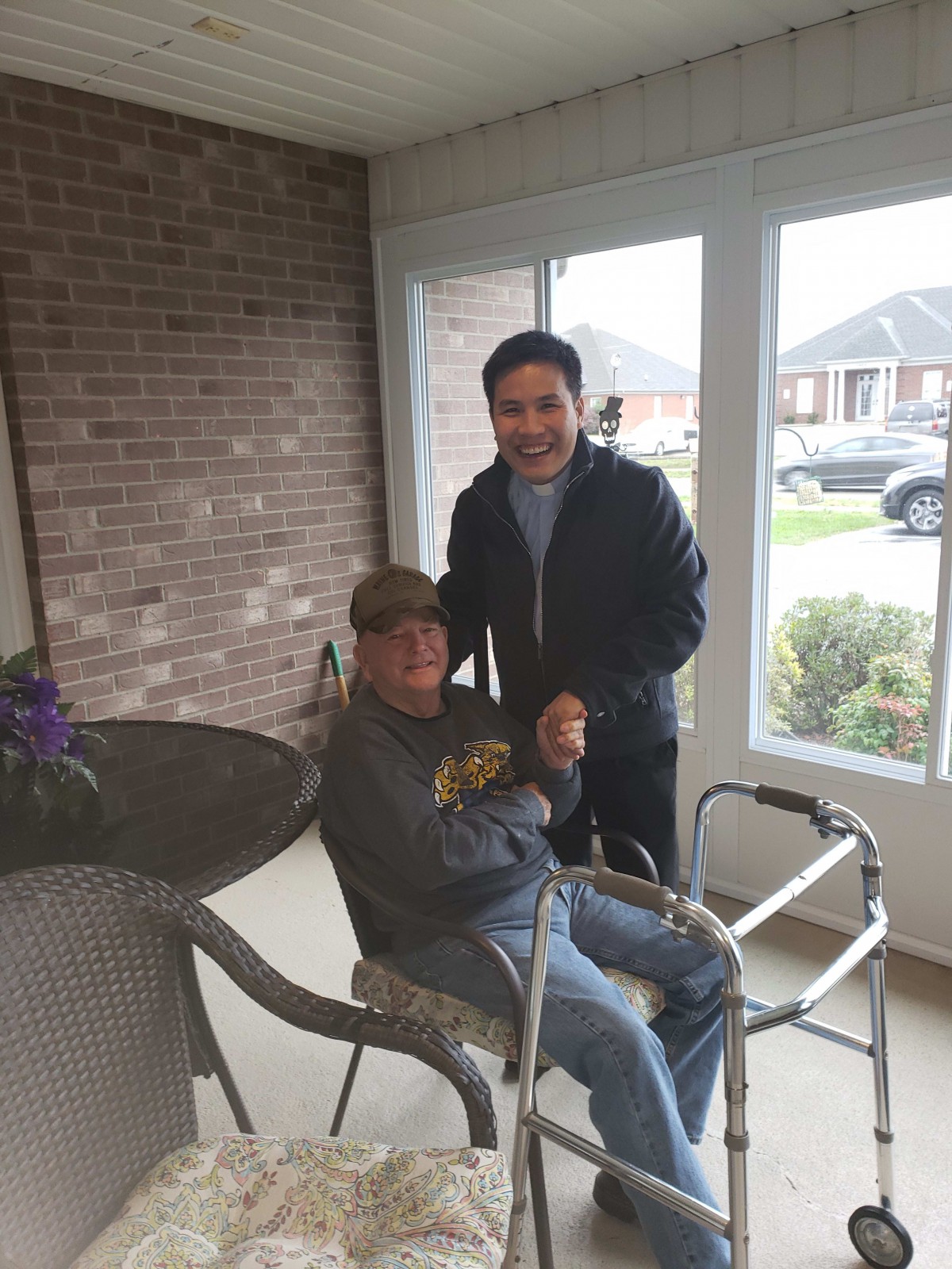 Two people smiling indoors, one seated with a walker.