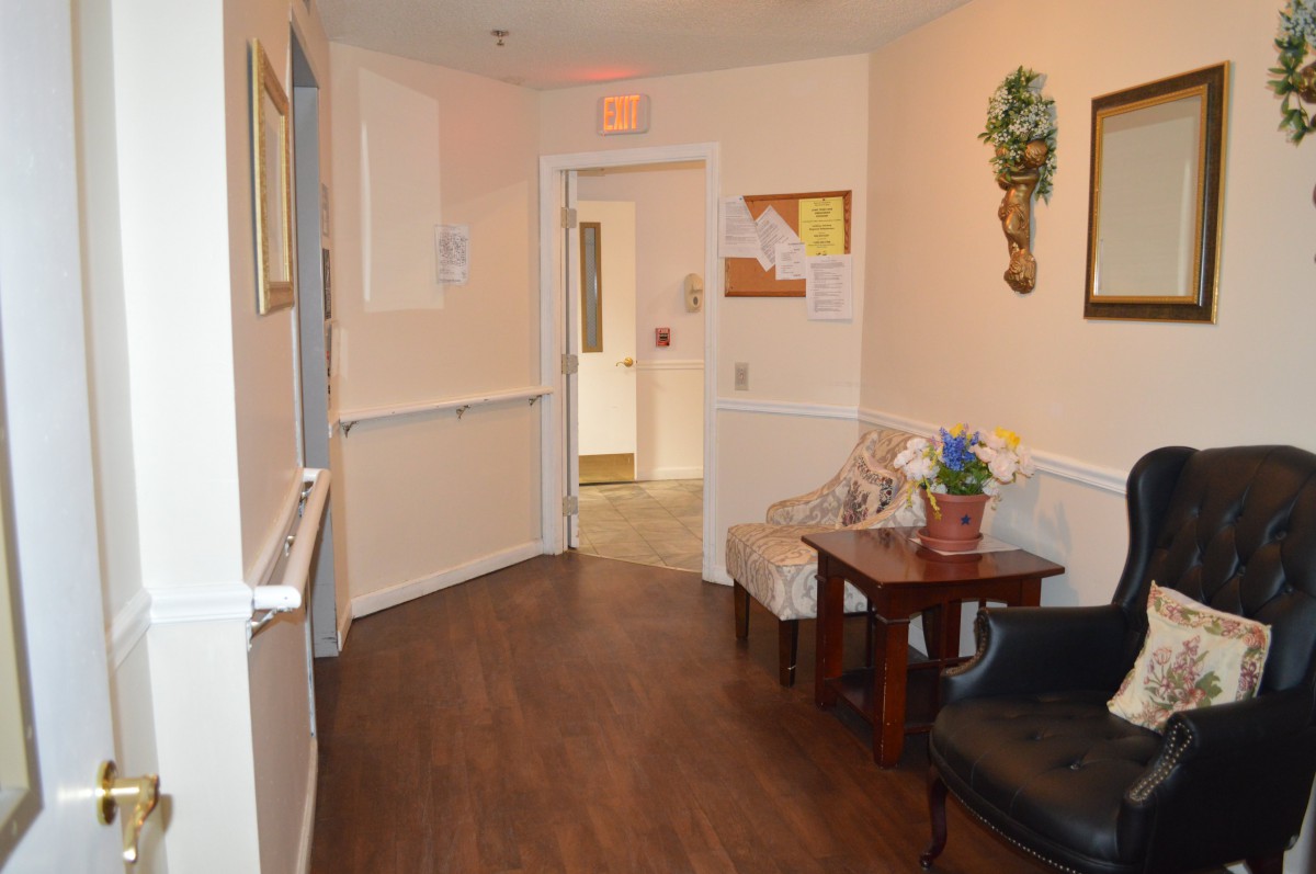 A hallway with wooden flooring, featuring a small seating area and decor along the walls.