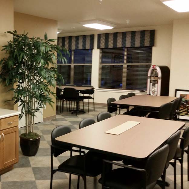 A cozy dining area with multiple tables and chairs, complemented by an indoor plant and a jukebox near the windows.