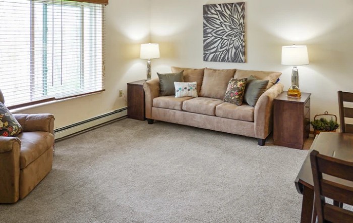 A cozy living room with a beige sofa, carpeted floor, and soft lighting from lamps.