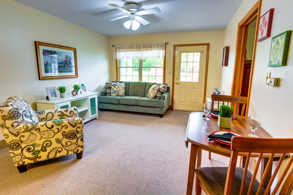 A cozy living room with a sofa, armchair, and coffee table, featuring natural light from a large window.