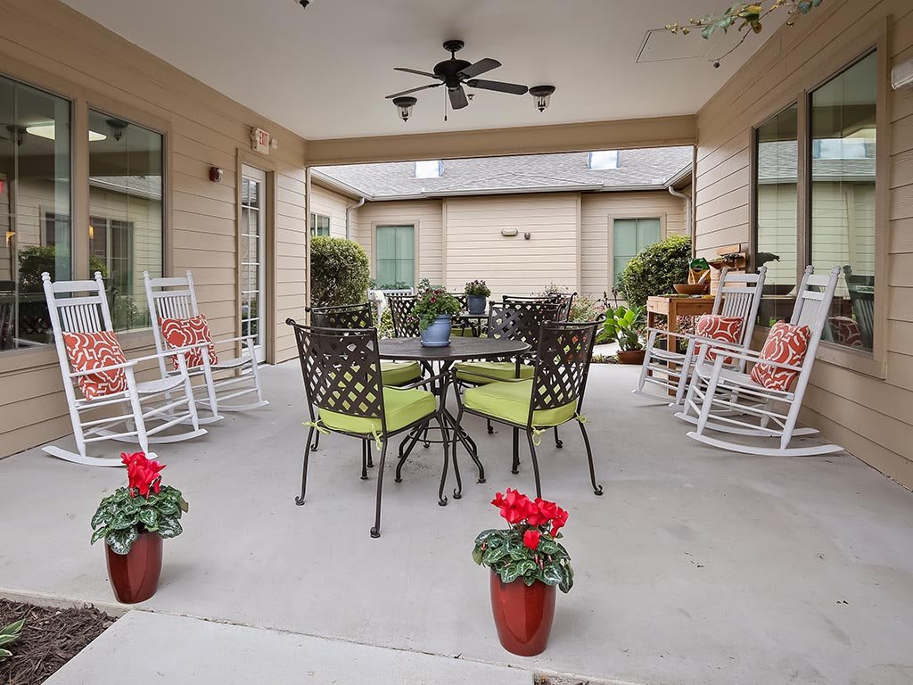 A cozy patio with rocking chairs and a table, surrounded by plants in a covered outdoor area.