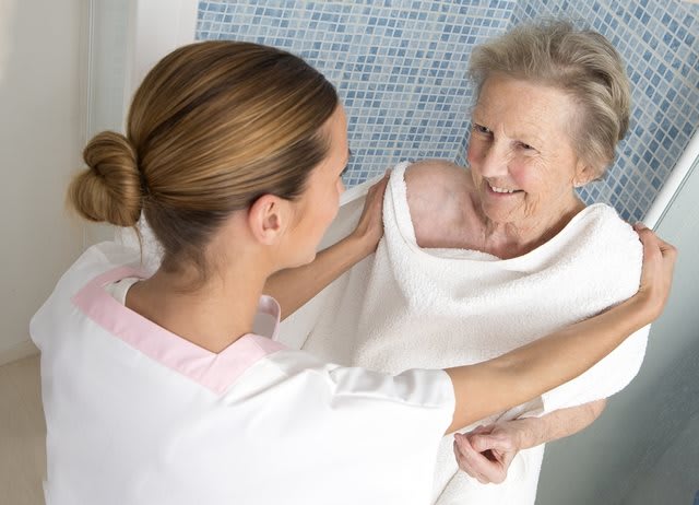 A caregiver assisting an elderly person with a warm smile and gentle care.