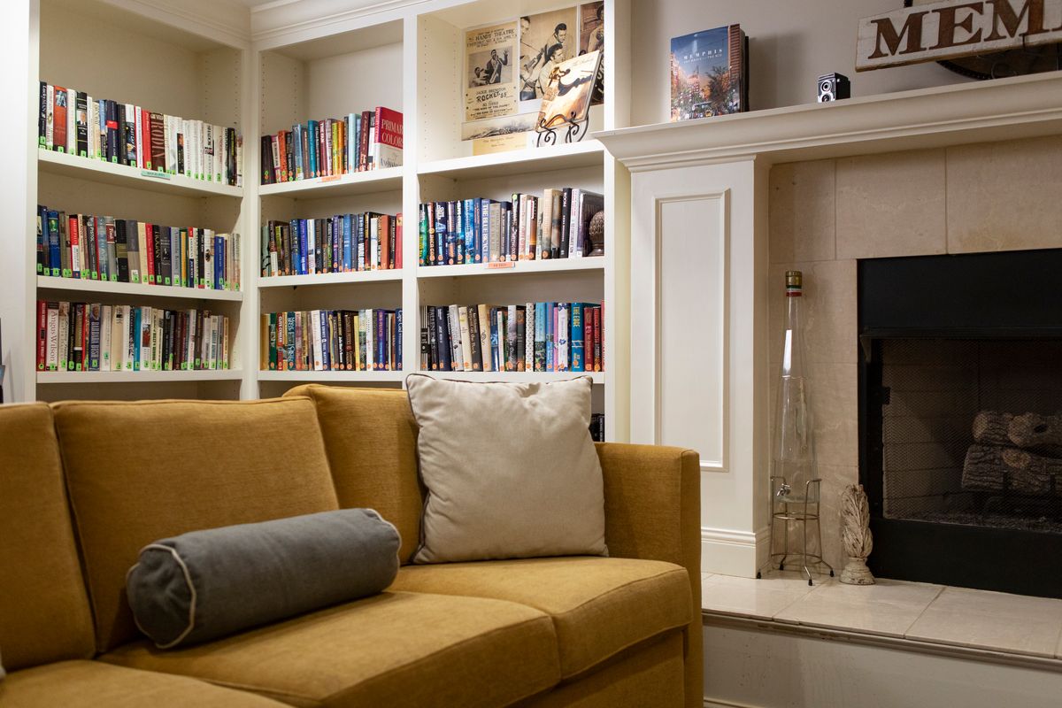 A cozy living room with a bookshelf filled with books, a yellow couch, and a fireplace.