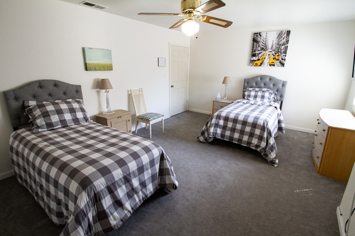 A cozy bedroom featuring two twin beds with checkered bedding, adorned with wall art and a ceiling fan.