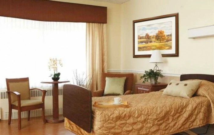 A well-decorated hospital room featuring a single bed, artwork, and a window with curtains.