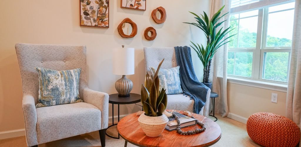 A cozy, modern living room with stylish armchairs, decorative wall art, and a coffee table adorned with books and a plant.