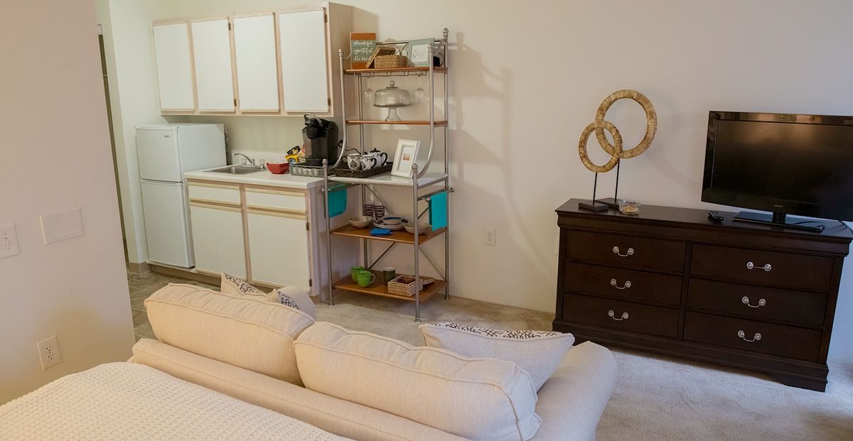 A cozy apartment interior featuring a small kitchen area with shelves and decorative items.