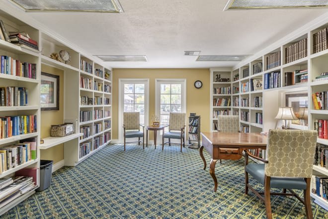 A cozy library reading room with bookshelves, chairs, and a table.