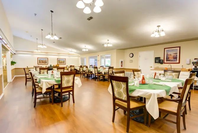 A spacious dining area with neatly arranged tables and chairs, featuring bright lighting and a wooden floor.