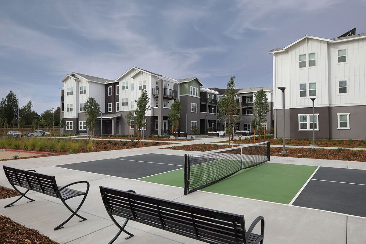 Modern apartment complex with a tennis court and outdoor seating.
