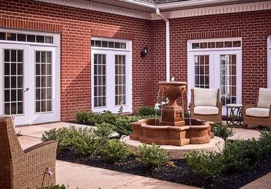 A charming courtyard with a central fountain, surrounded by a brick building and well-maintained garden spaces.