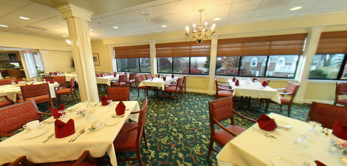 A well-lit restaurant dining area with neatly arranged tables and chairs, carpeted flooring, and large windows.