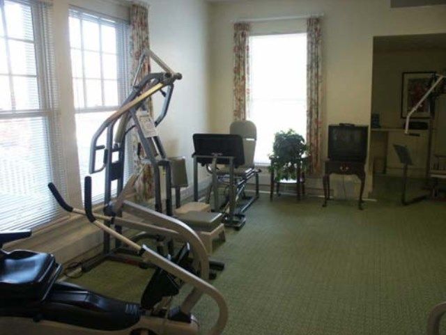 A home gym with exercise equipment and chairs in a bright room.