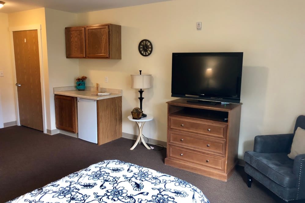 A cozy hotel room with a television, mini fridge, and wooden furniture.