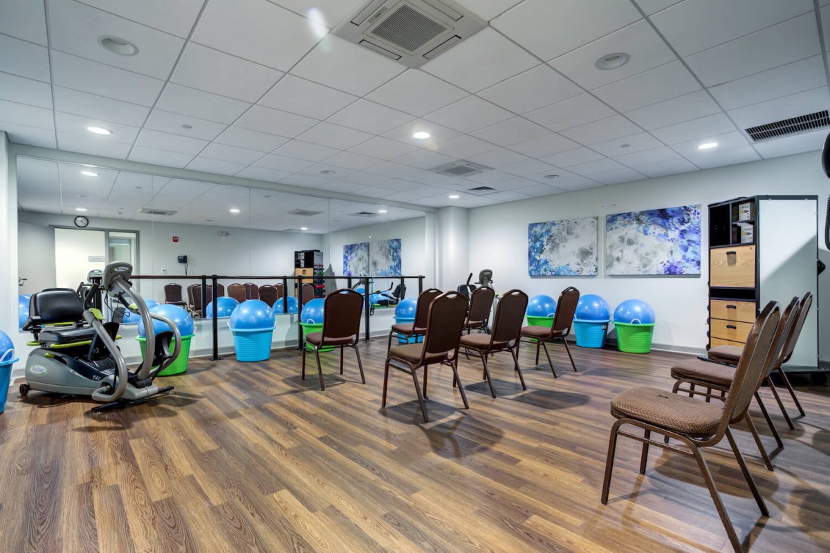 A fitness room equipped with exercise chairs, gym balls, and mirrors on a wooden floor.