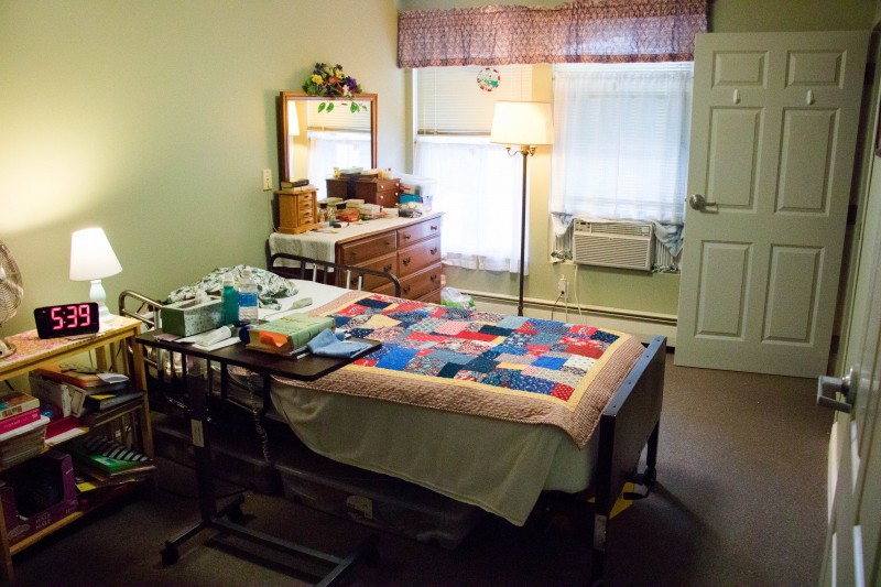 A cozy bedroom with a quilt-covered bed, dresser, and soft lighting from a floor lamp.