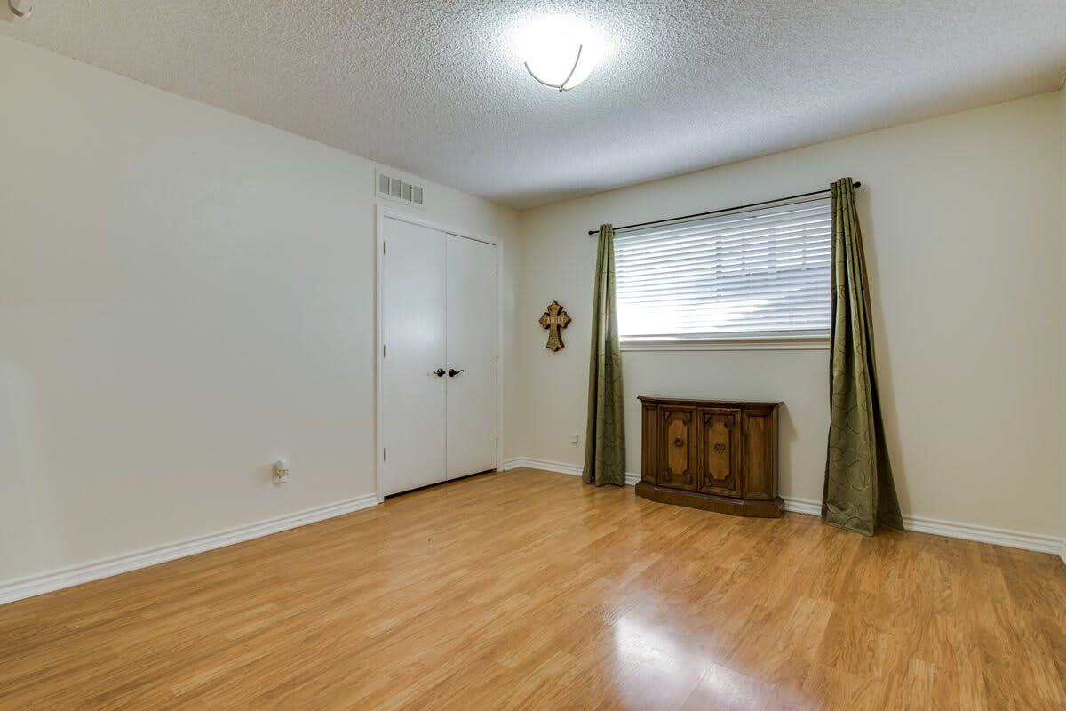 An empty room with wood flooring, green curtains, and a decorative piece under the window.