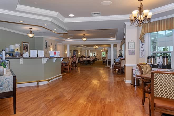 A spacious and well-lit lobby area with wooden flooring, chandeliers, and a reception desk.
