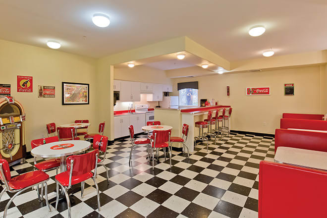 A retro-style diner with red and white decor, featuring a checkerboard floor and bar stools.