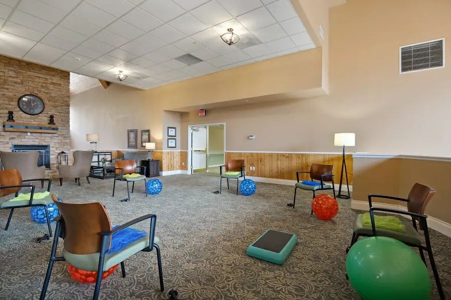 A well-lit exercise room with chairs and colorful exercise balls arranged on a carpeted floor.