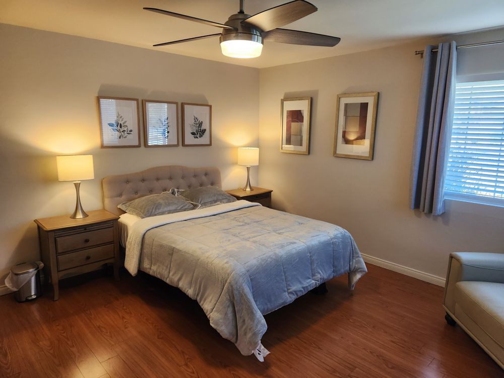 A cozy bedroom featuring a neatly made bed, decorative lamps, and framed artwork on the walls.