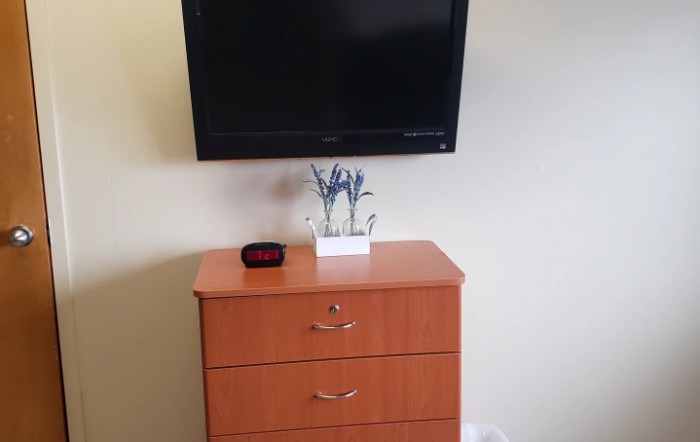 A minimalist setup with a wall-mounted TV above a wooden dresser, adorned with a small plant and decorative item.