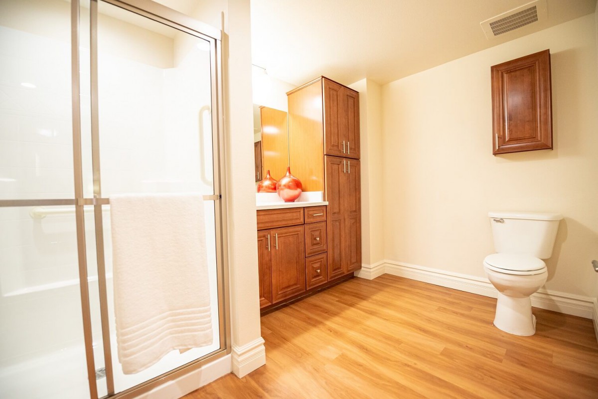 A spacious bathroom with wood flooring, featuring a shower and wooden cabinetry.