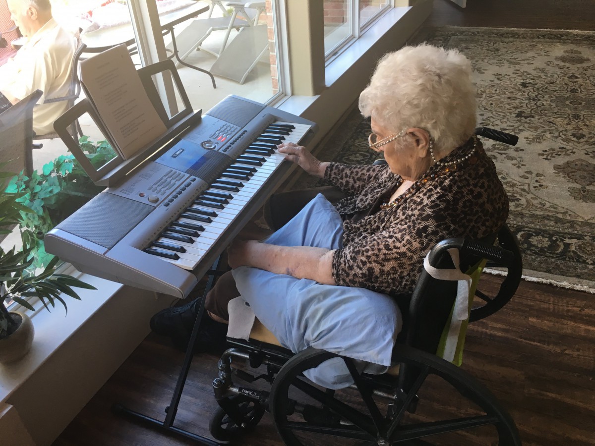 An elderly woman playing a keyboard while sitting in a wheelchair.
