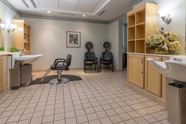 An empty hair salon with styling chair, dryer chairs, and tidy cabinets.