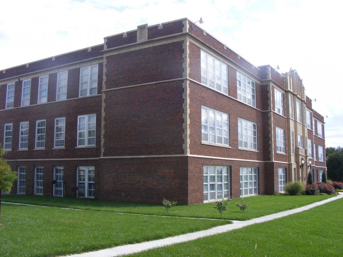 A three-story brick building with large windows and a surrounding lawn.