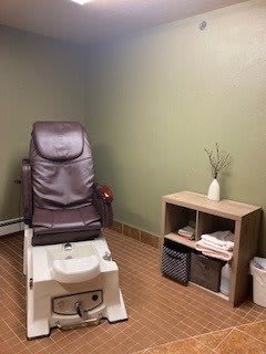 A cozy spa room featuring a pedicure chair and a small shelf with neatly arranged towels and decor.