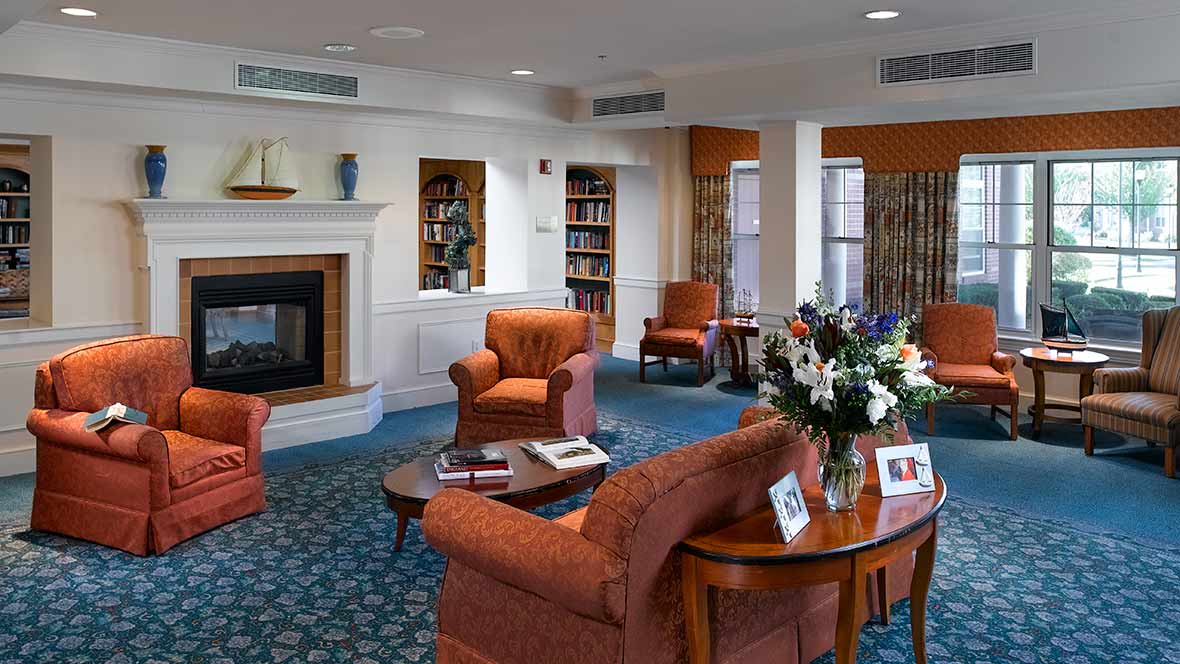A cozy living room with armchairs and a fireplace, featuring bookshelves and a floral arrangement on the coffee table.
