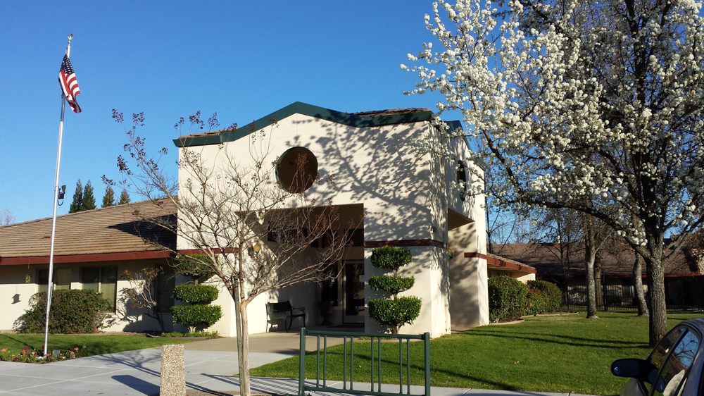 A quaint church surrounded by green lawns and blossoming trees under a clear blue sky.