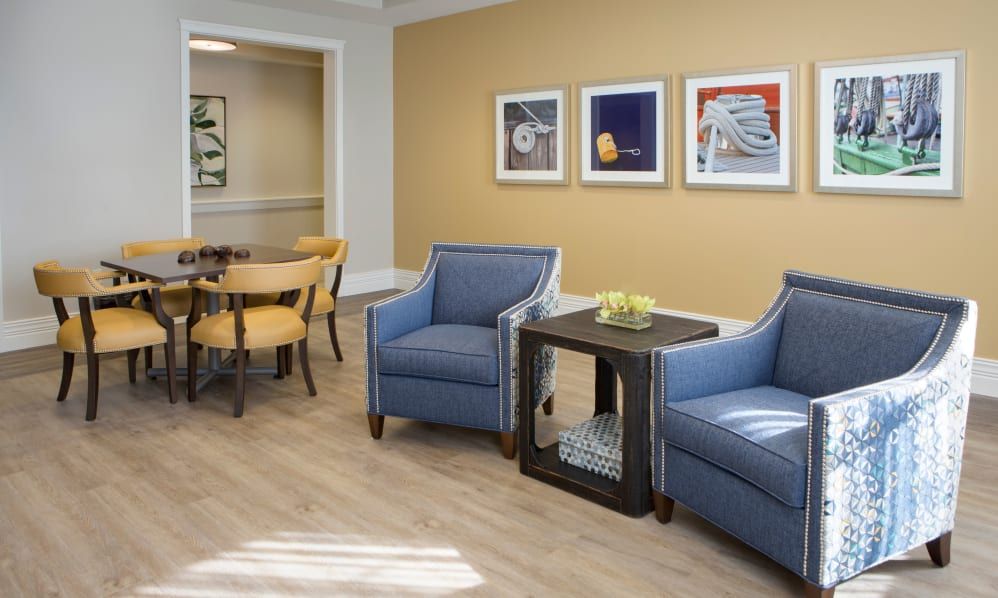 A cozy living room with blue armchairs, a small table, and framed artwork on the walls.