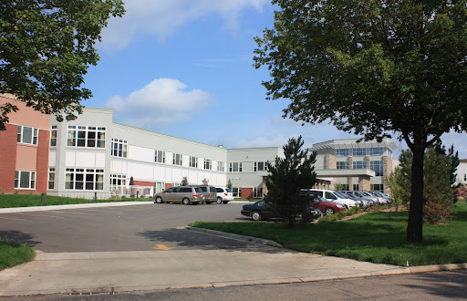 An outdoor view of a modern office building with a spacious parking lot surrounded by trees.