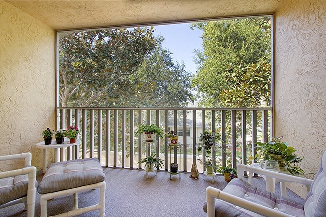 A cozy balcony with comfortable seating and lush potted plants offers a serene view of the surrounding trees.