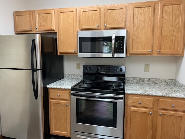 A modern kitchen featuring stainless steel appliances, wood cabinets, and a granite countertop.