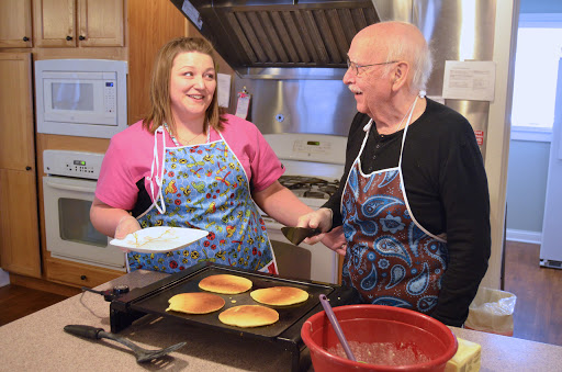 A joyful moment in the kitchen as two individuals share a laugh while making pancakes together.