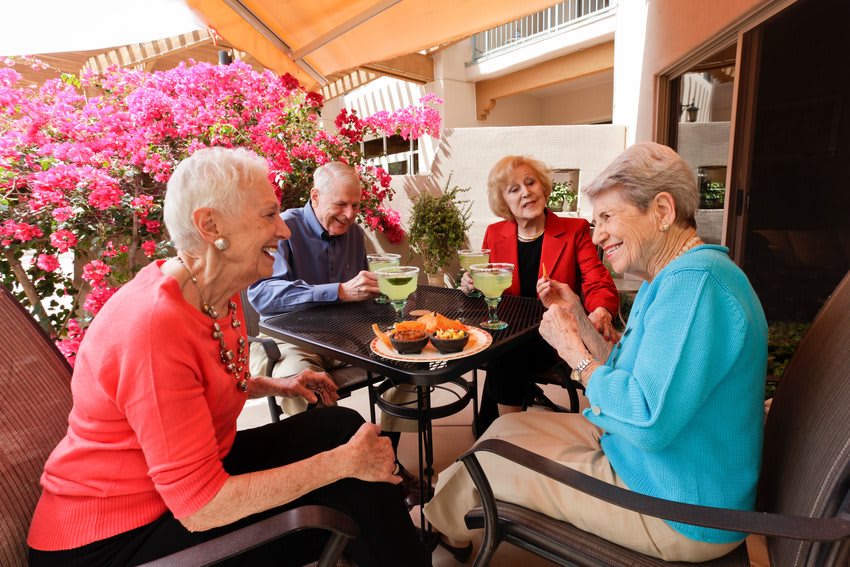 A group of seniors enjoying a lively conversation over drinks at an outdoor patio.