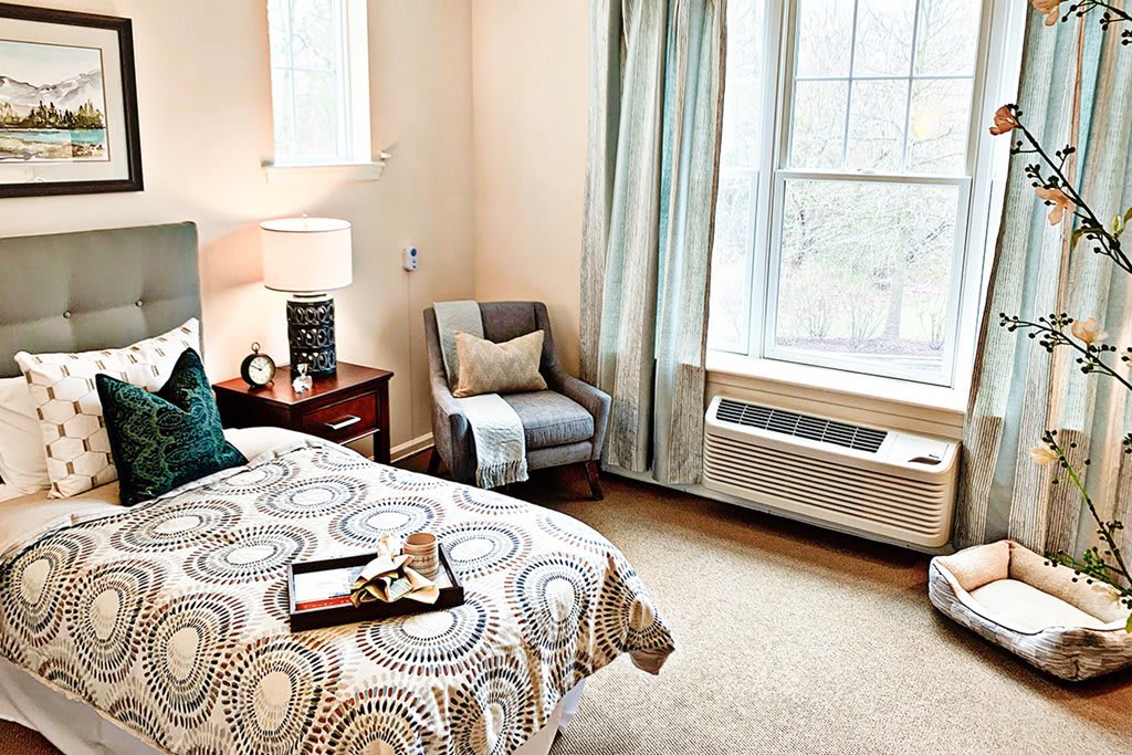 A cozy and well-lit bedroom with a patterned bedspread, armchair, and large window.