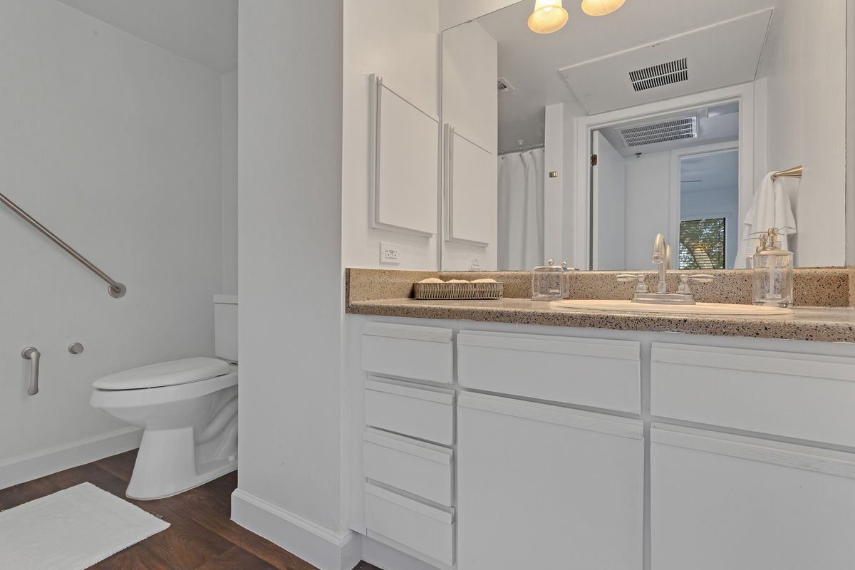 A modern bathroom with white cabinets, a sink, and a mirror next to a toilet.