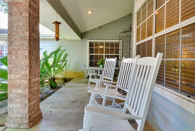 A cozy porch with white rocking chairs and lush greenery.