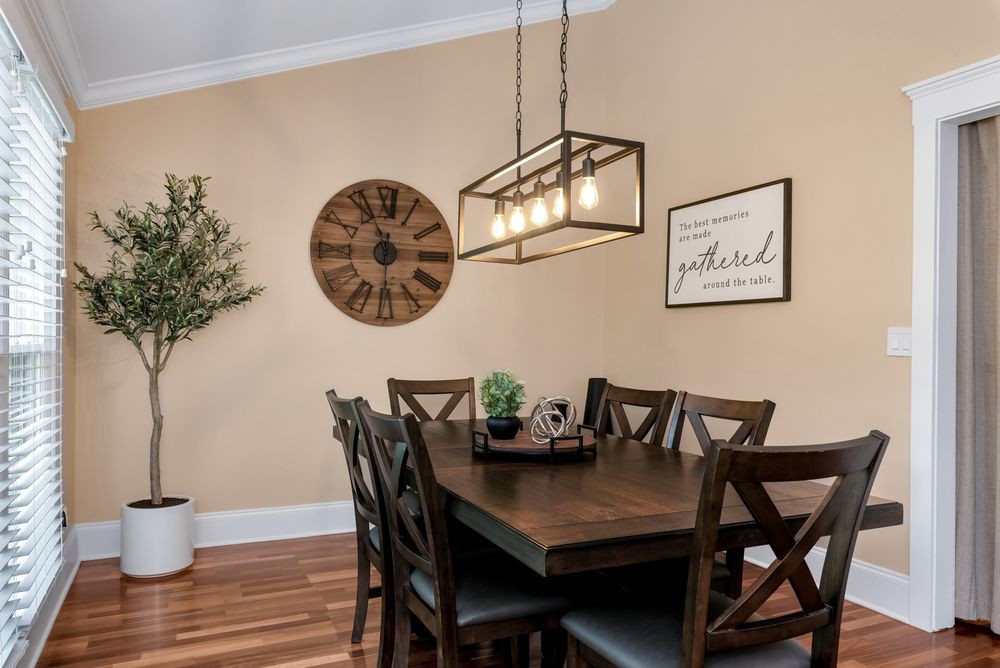 A cozy dining room with a wooden table and chairs, featuring a pendant light and decorative elements like a wall clock and a potted plant.