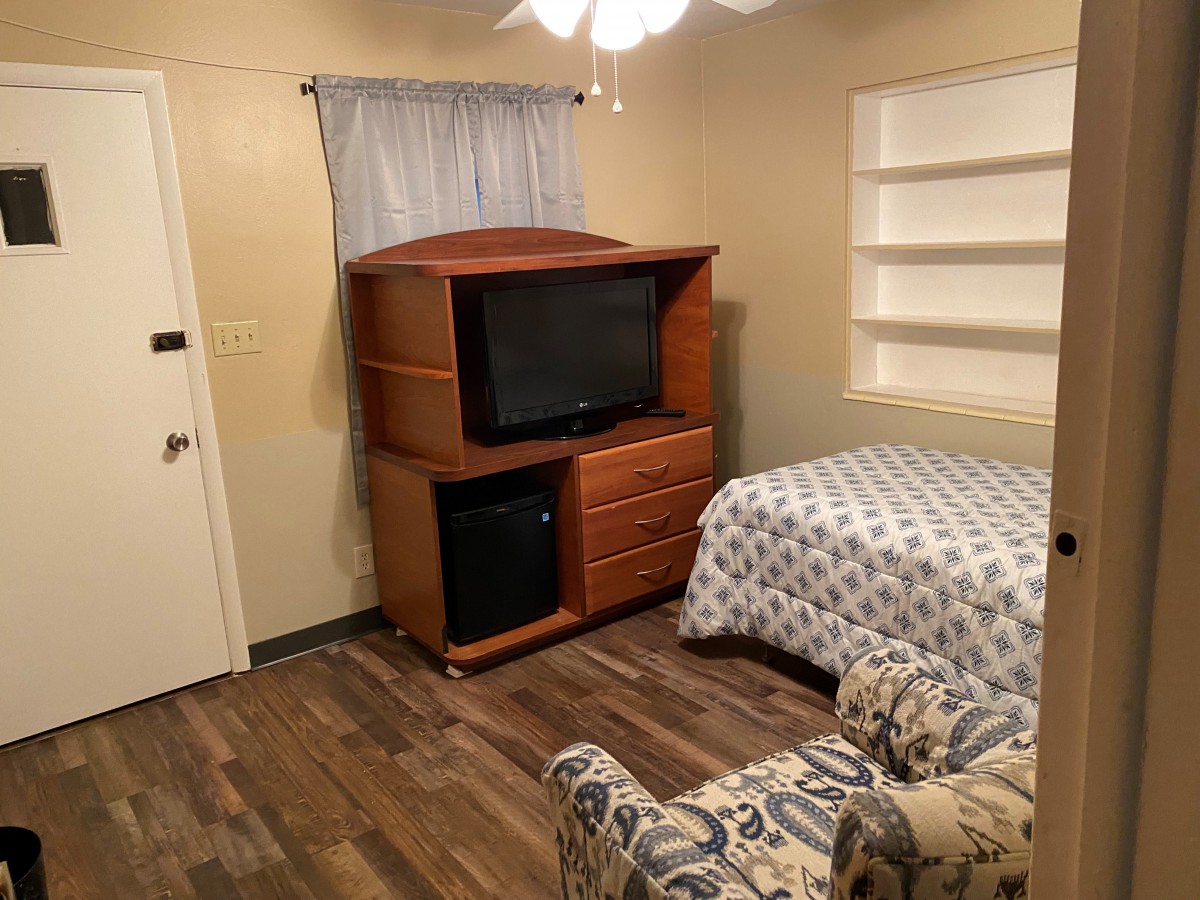 A cozy bedroom with a television, bed, and armchair.