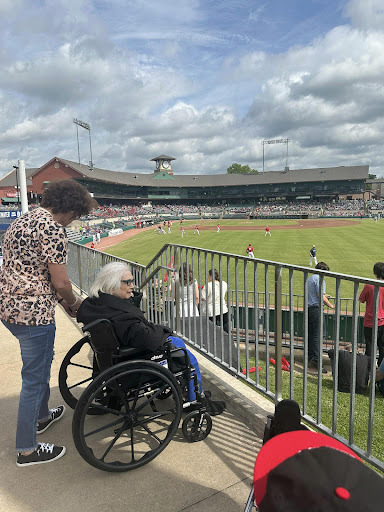 An elderly person in a wheelchair enjoying a baseball game with a companion at the stadium.
