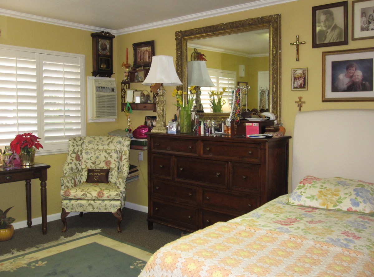 A cozy bedroom featuring a dresser with a large mirror, surrounded by decorative elements and a floral armchair.
