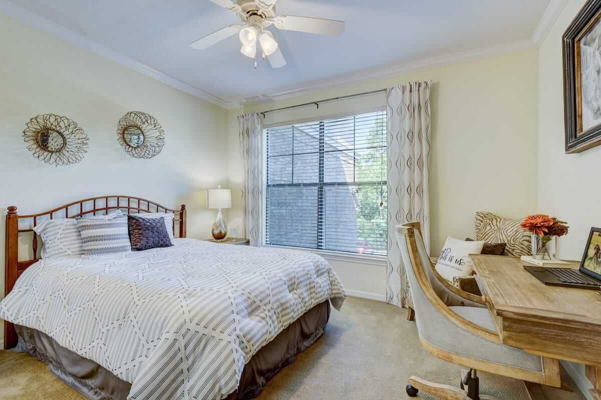 A cozy bedroom with a neatly made bed, a desk by the window, and tasteful decor.