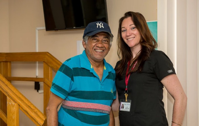 Two people smiling indoors, one wearing a striped shirt and cap.