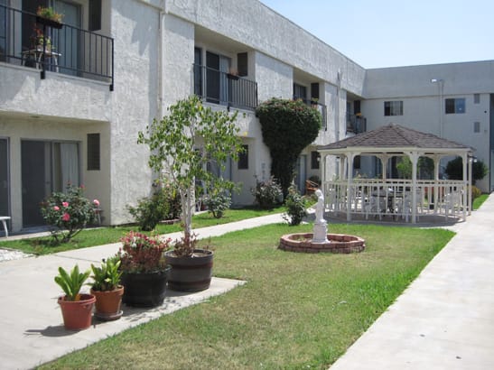 A well-maintained apartment complex courtyard featuring a gazebo, greenery, and a pathway.
